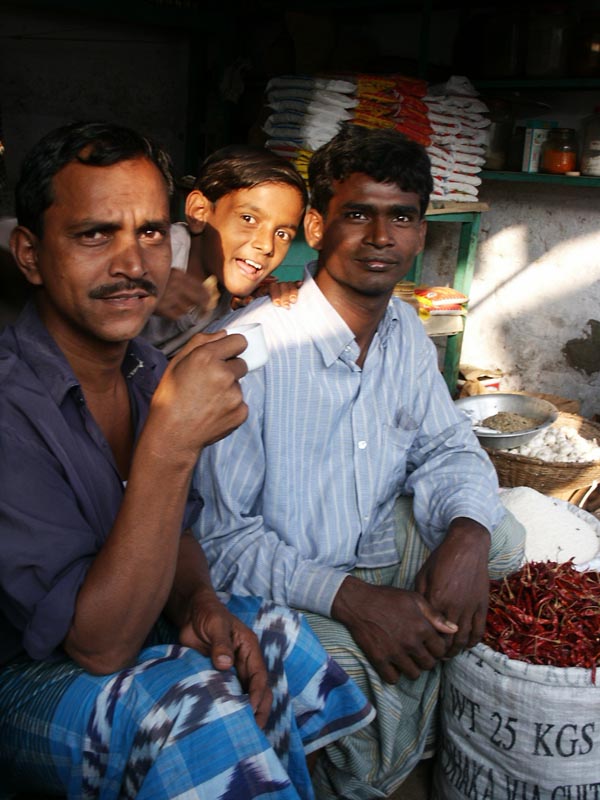 Boy lit up with 2 men at produce market, Dhaka