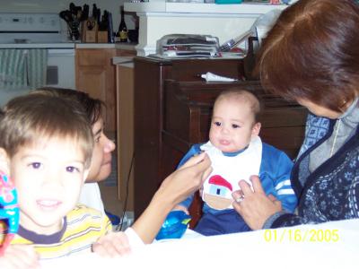 Tricia feeding Evan his first bite of rice cereal, while Lola holds him and Ben watches