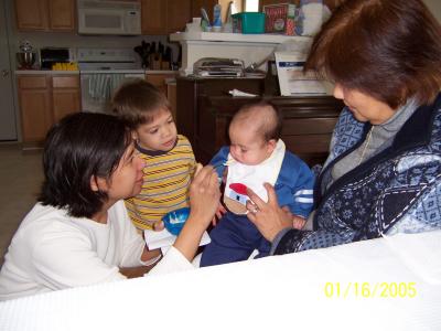 Tricia feeding Evan his first bite of rice cereal, while Lola holds him and Ben watches