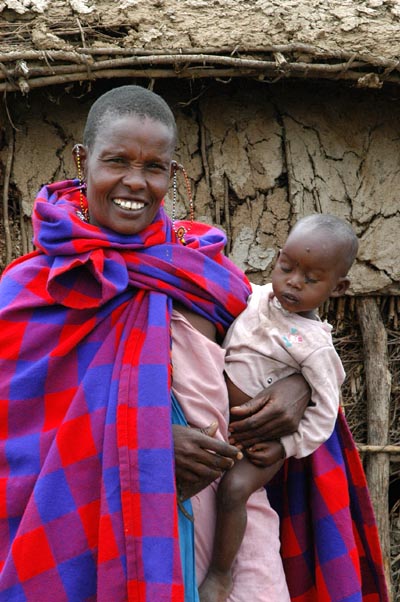 Maasai woman and child in front of one of the huts