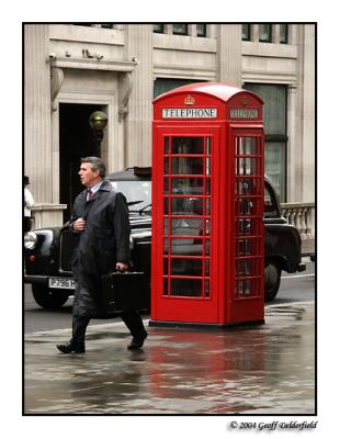 businessman walks past traditional red telephone box
