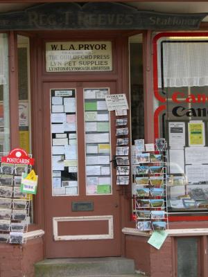 If you look at the original size, you can make out that this door is

W.L.A. Pryor
Trading as:
The Guildford Press
Lyn Pet Supplies
Lynton and Lynmouth Advertisers

I just loved the clutter. The first time I passed this door the shop was closed but with the post cards still sitting out. There was a sign on the door asking buyers to drop the post card money thru the mail slot