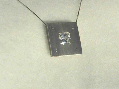 A 10mm square cubic zirconia is rivetted between 2 sheets of silver.  The pendant is 25mm square in total, and can be suspended from one or 2 rivets (see next photo also).  SOLD