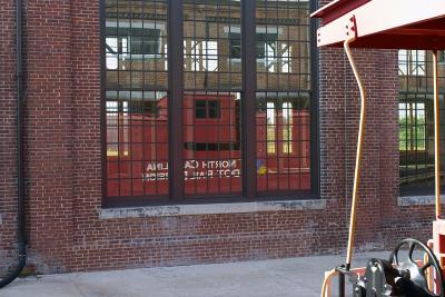 A caboose reflected in one of the Back Shop's windows. The caboose is open so that visitor can walk through it.