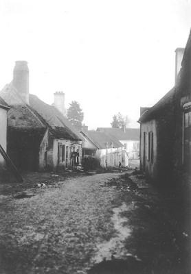 OLD PHOTO   # 8, Village view, with open drains.  Woman in distant doorway on the left.