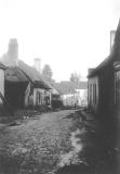 OLD PHOTO   # 8, Village view, with open drains.  Woman in distant doorway on the left.