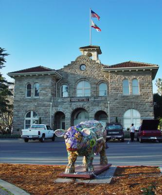 Spotted tethered to the flag pole in front of City Hall, Udderly Sonoma gazes over a fountain. Animal Rights Activists are upset that Udderly Sonoma is too far to get a drink of water and is charging City Hall with cruelty to animals. Udderly Sonoma was given her identity by Jan Hansen in 2001. She was cloned by William Kreysler & Associates near Petaluma, CA who specializes in molds and finished fiber-resin sculptures for sculptors and architects worldwide. The original bodacious bovine was carved from a large block of pink styrofoam. Nine body pieces make up each cow. When assembled each cow is carefully seamed together and filed down before getting a gel set coating, and then a coat of white paint. Potential artists are given a coloring book like sheet of paper and are invited to decorate a cow. Sponsors look among the winning designs and pick an artist to complete the decoration of a cow mold. Also available for decoration are four feet high Plaza Chickens which remained hidden from this photographer's view.