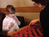 Vicki is four years old.  She is learning to play checkers for the first time.  Katie is teaching her how.