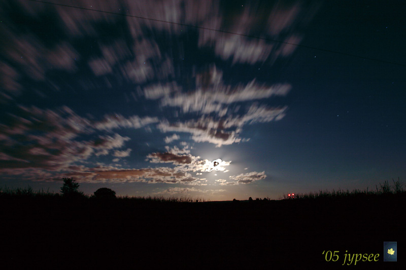 green corn moon emerging from moving clouds