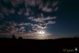 green corn moon emerging from moving clouds