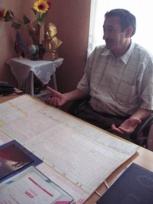 Candid photo of the director.  On his desk is a large, hand-written schedule for the whole school.